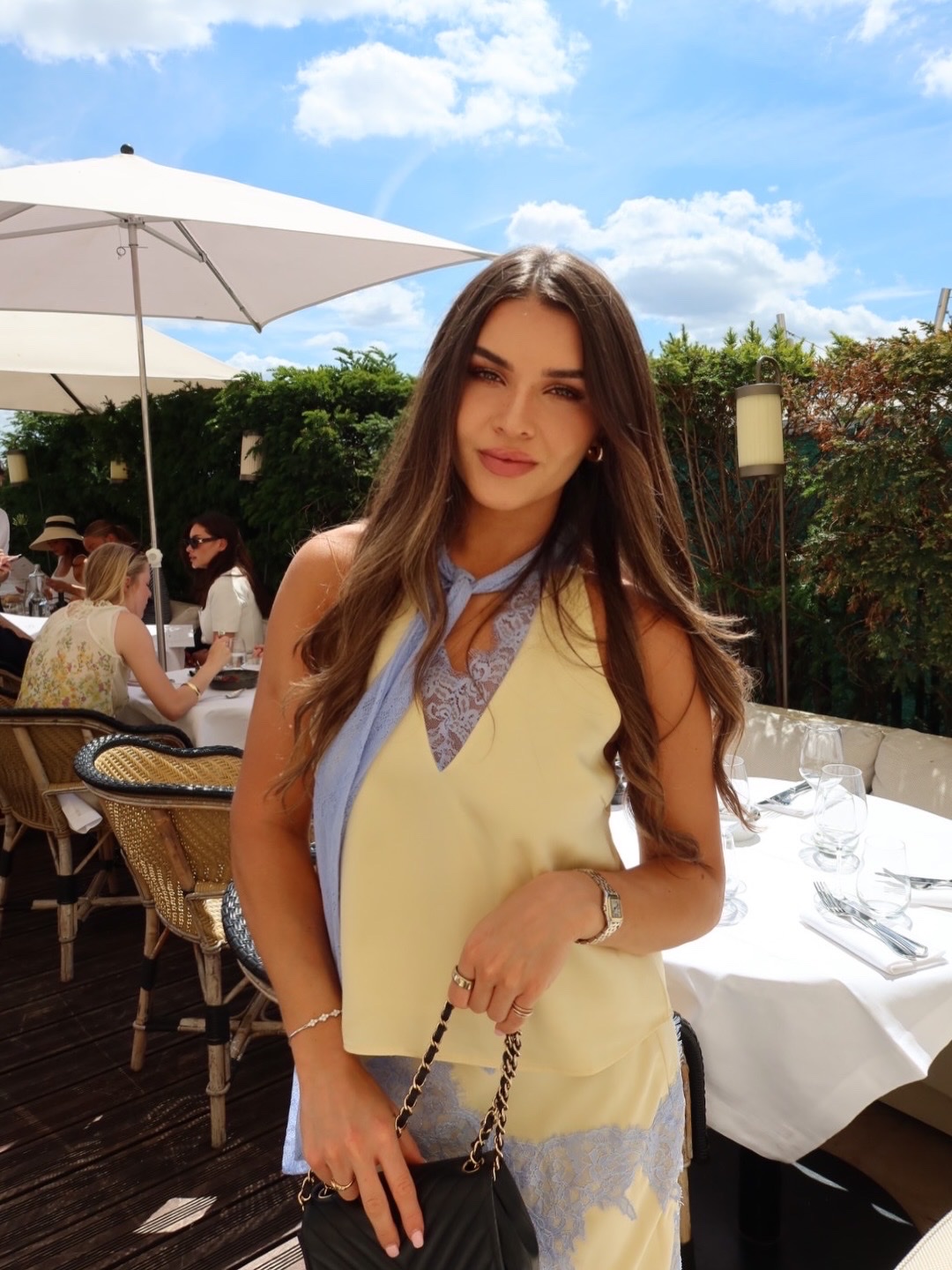 Jess in a pastel yellow and blue outfit at an outdoor restaurant