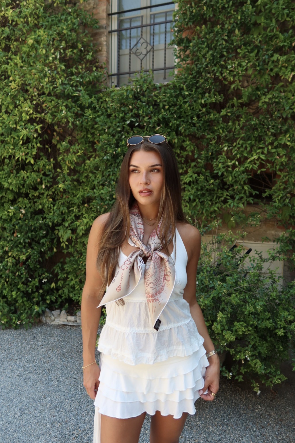 Jess in a white summer dress standing in front of an ivy-covered wall