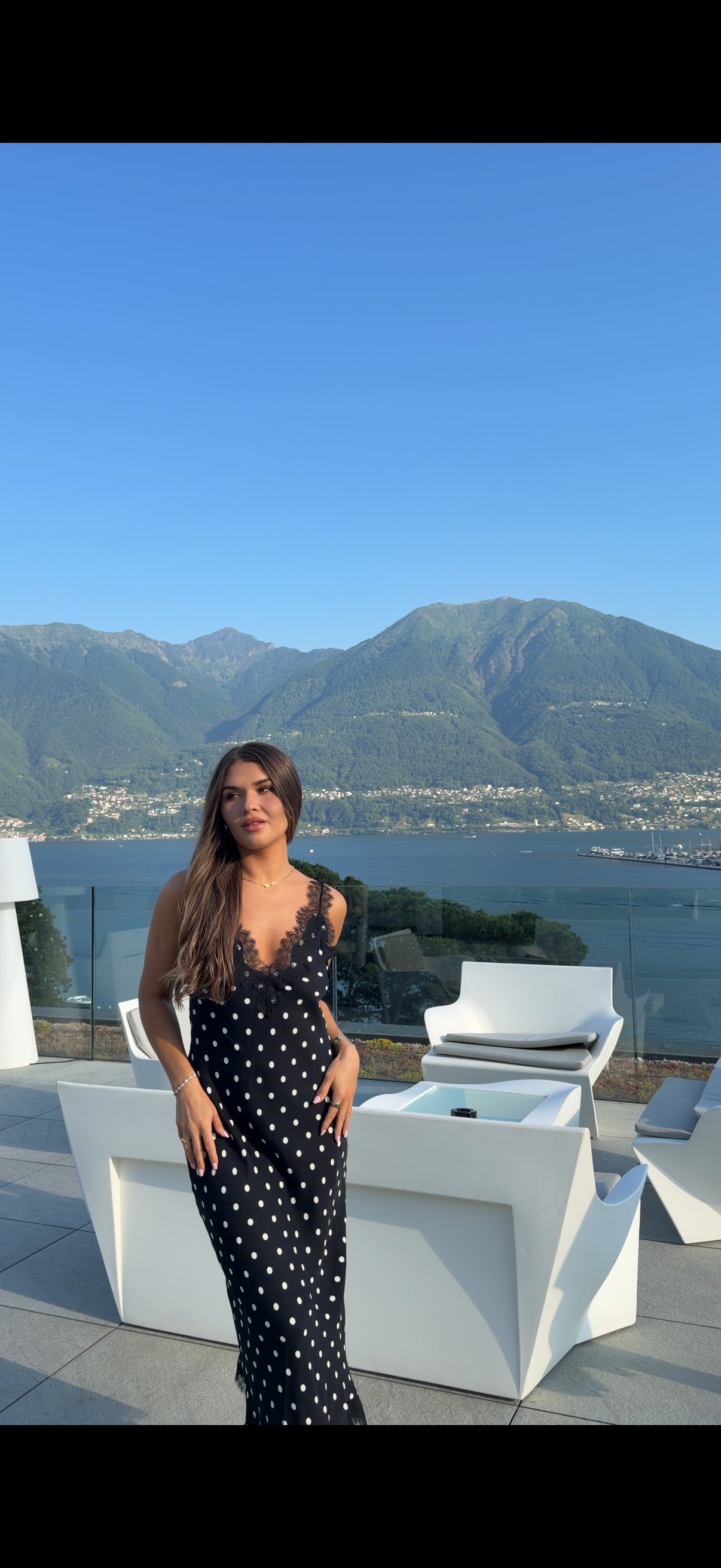 Jess in a polka dot dress on a terrace overlooking a lake