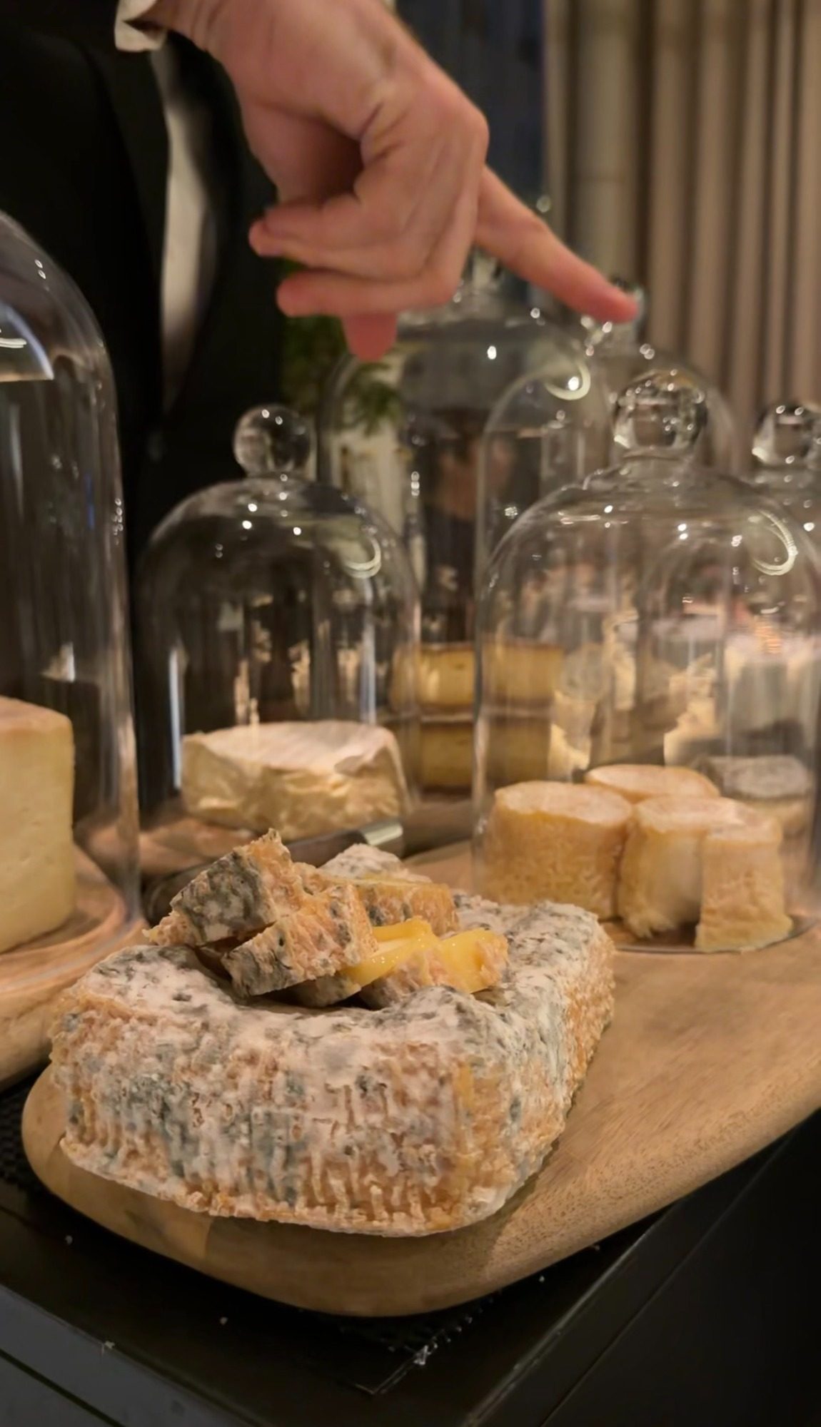 Blue cheese and other cheeses under glass cloches at Restaurant Alliance, with a server pointing