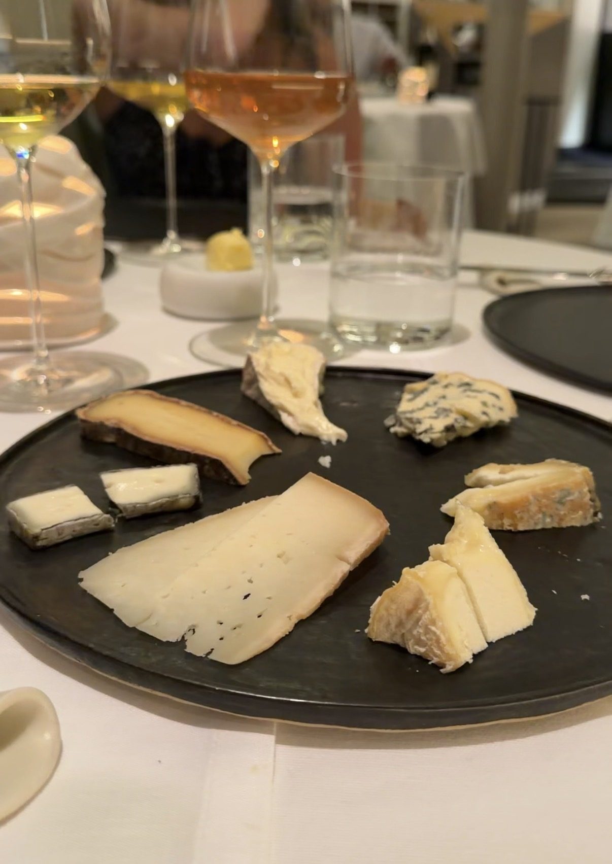 A black plate of several cheeses with white and rosé wine at Restaurant Alliance Paris