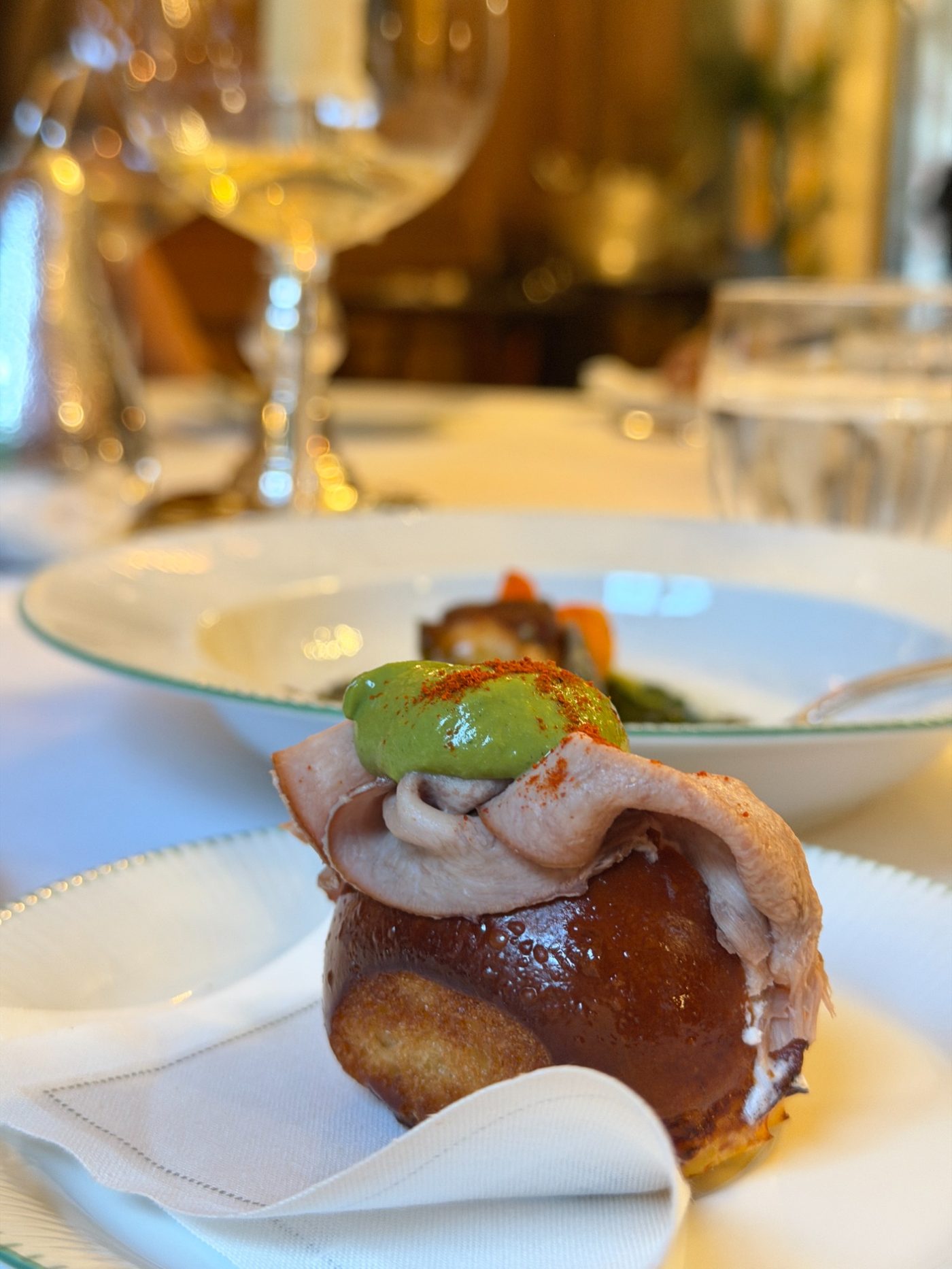 A glazed bun filled with sliced meat and green sauce at Le Clarence