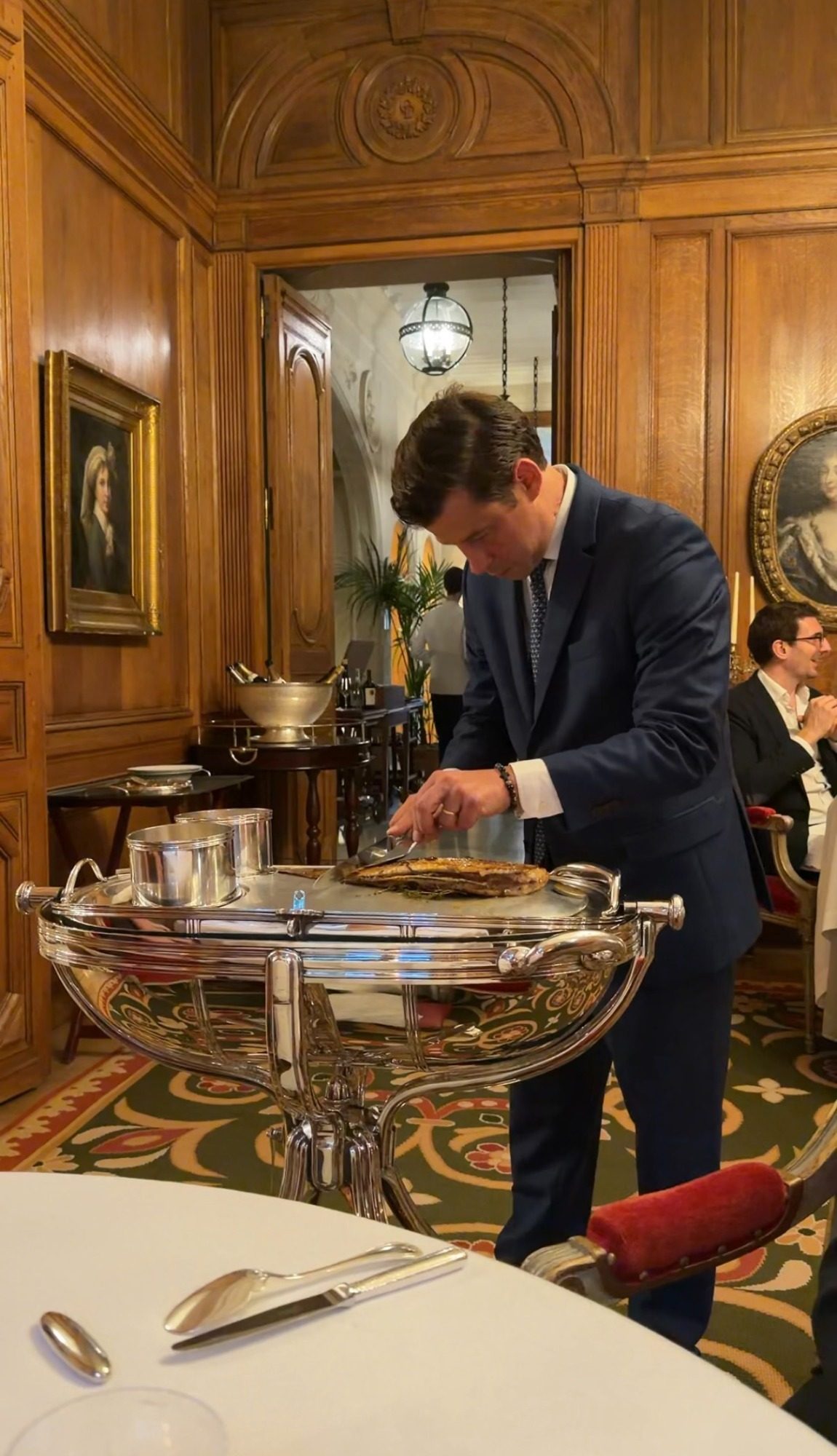 A server carving fish from a silver trolley in the wood-paneled dining room at Le Clarence