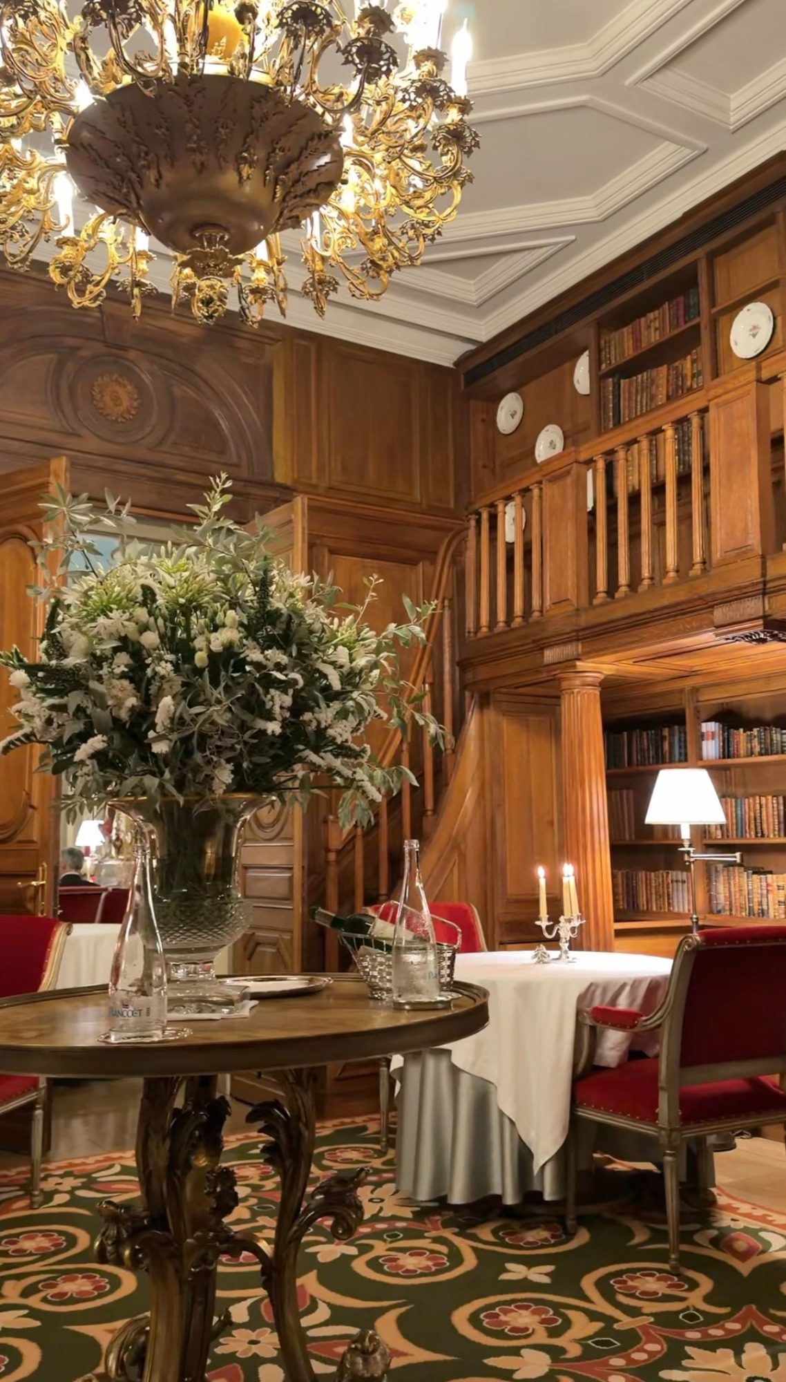 White flowers, a chandelier, and a set table in the library at Le Clarence Paris