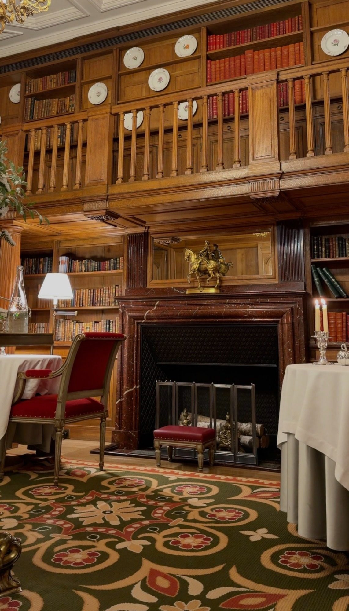 The library dining room at Le Clarence, with bookshelves, a marble fireplace, and red chairs