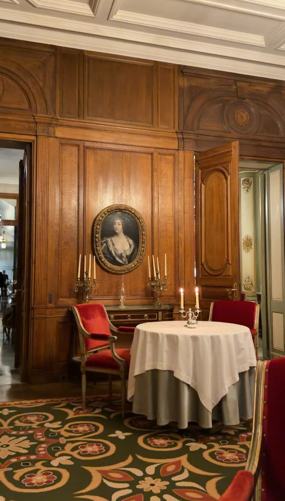 A round table and red velvet chairs in a wood-paneled dining room at Le Clarence in Paris, with candles and an oval portrait