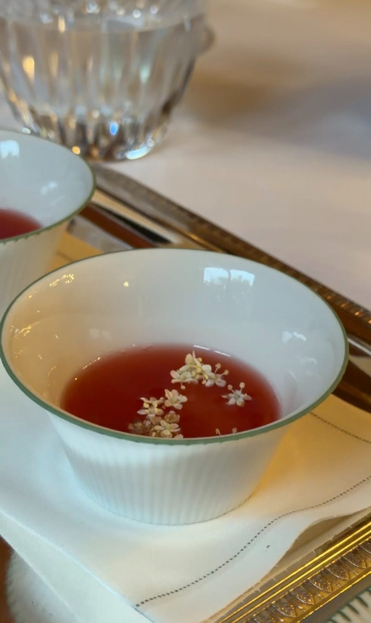 A cup of red broth with small white flowers at Le Clarence Paris
