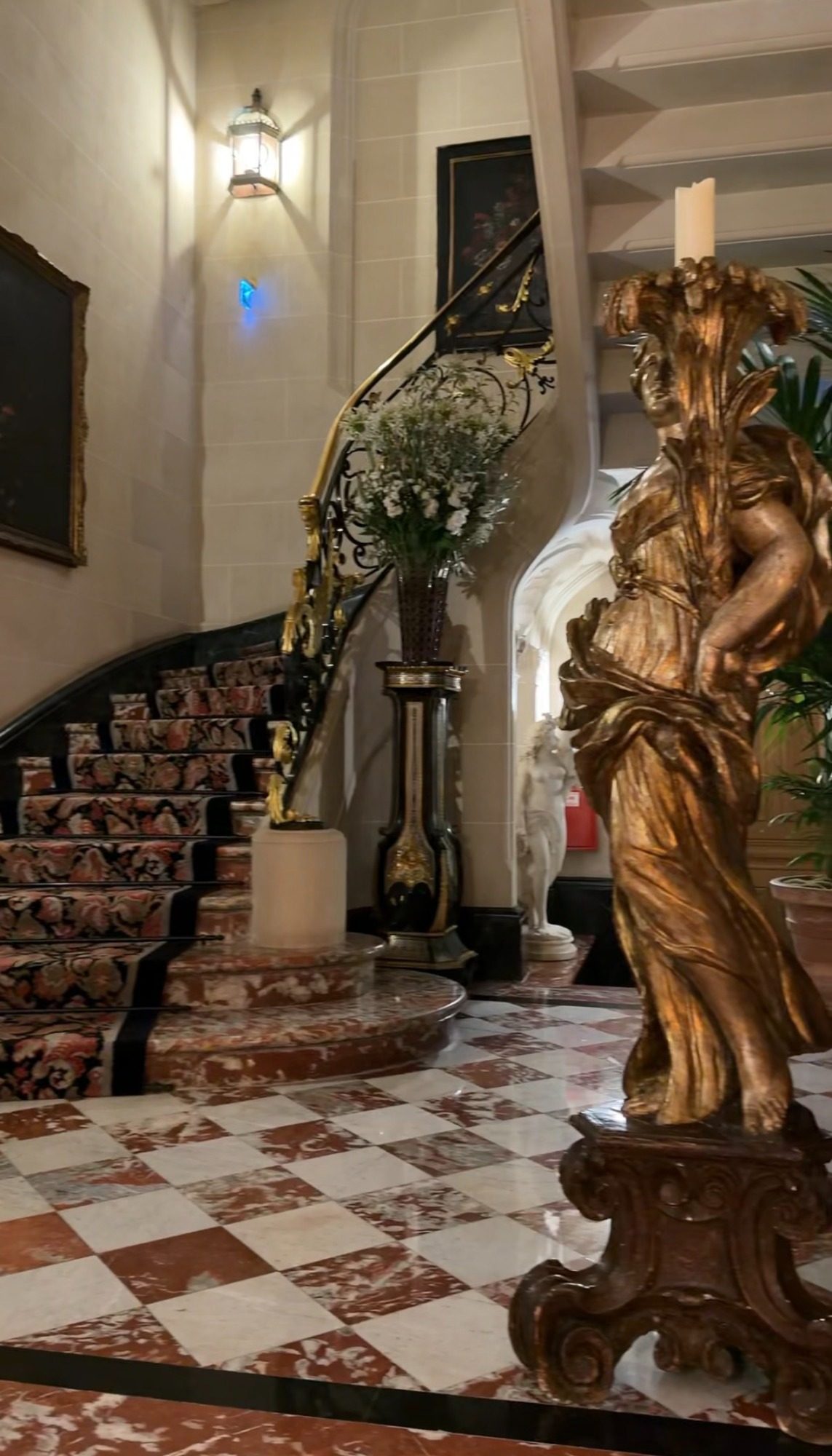 The spiral staircase at Le Clarence in Paris, with a floral carpet, checkerboard marble, and a gold statue