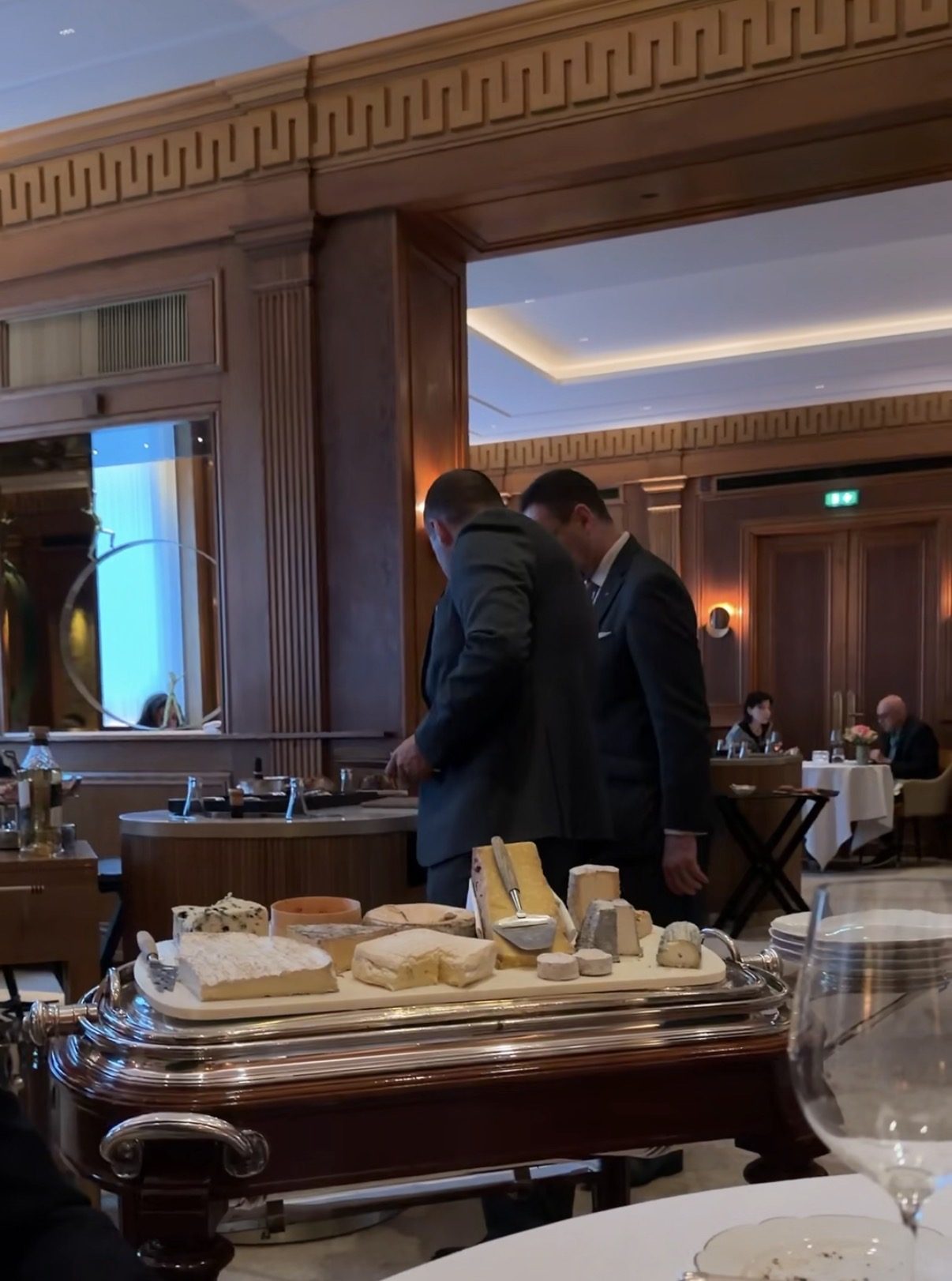 Servers with the cheese trolley in the wood-paneled dining room at Le Taillevent