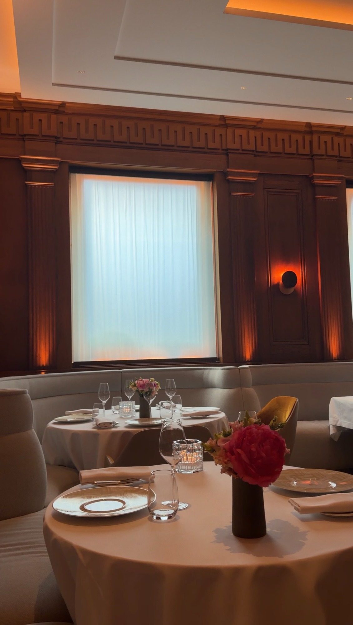 Le Taillevent dining room in Paris, with a pink peony on a set table and wood paneling around a tall window