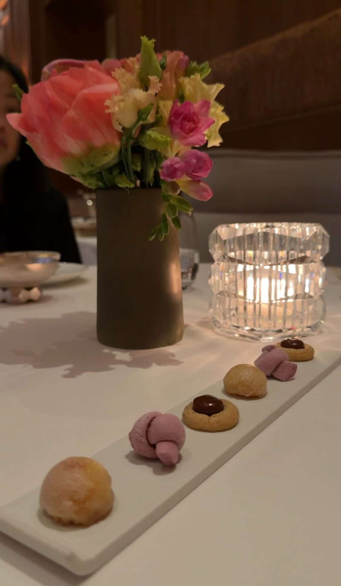 Petit fours on a long white plate at Le Taillevent, with flowers in a dark vase