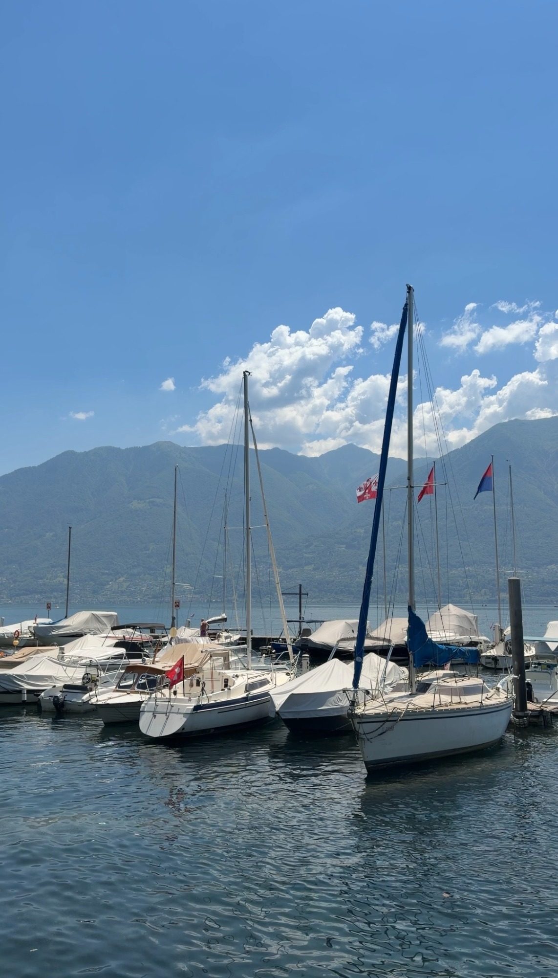 Sailboats on Lake Maggiore in Locarno, Switzerland, with mountains behind the harbor