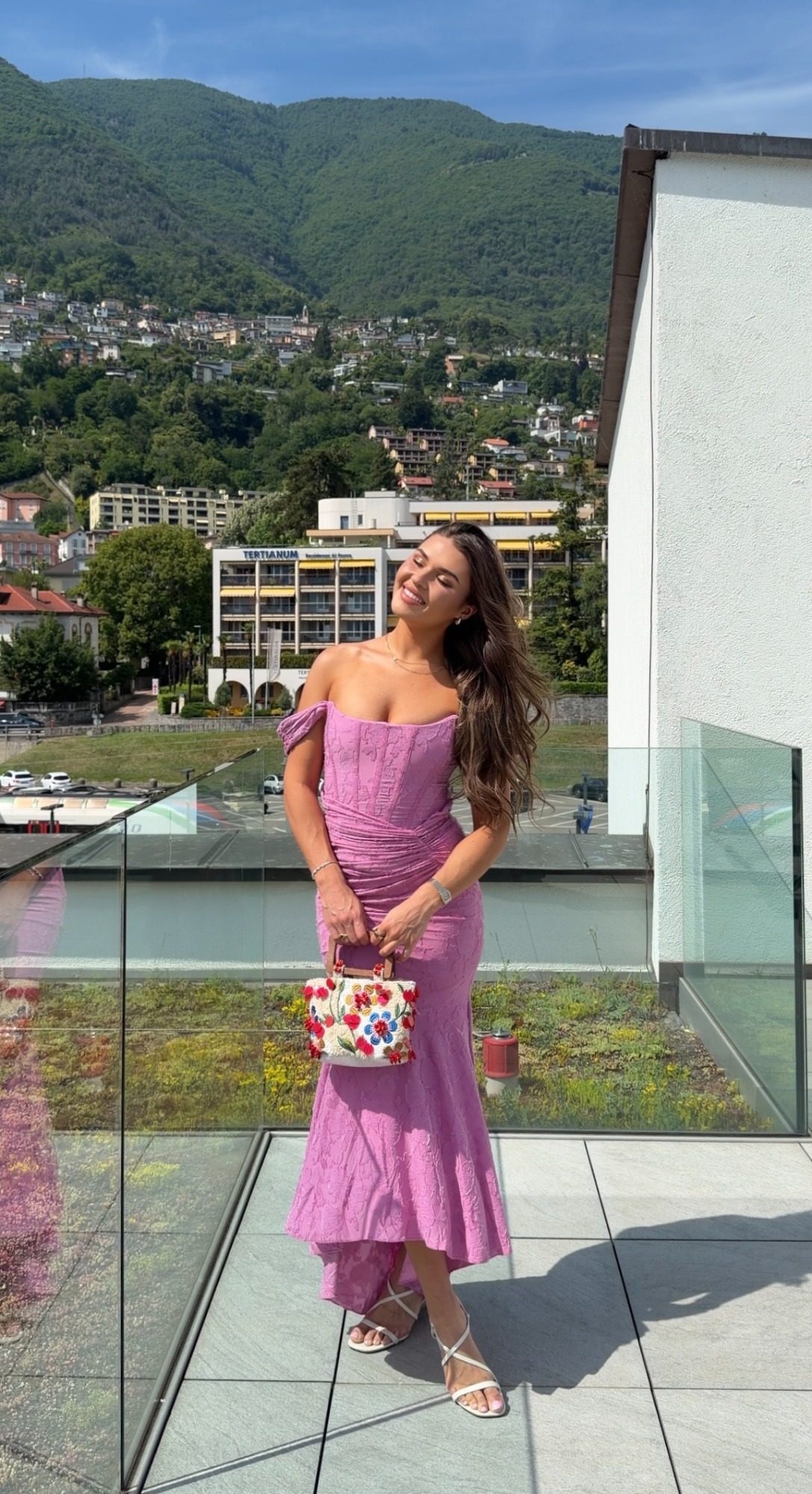 Jess in a pink dress on a glass terrace overlooking Locarno and the Swiss mountains
