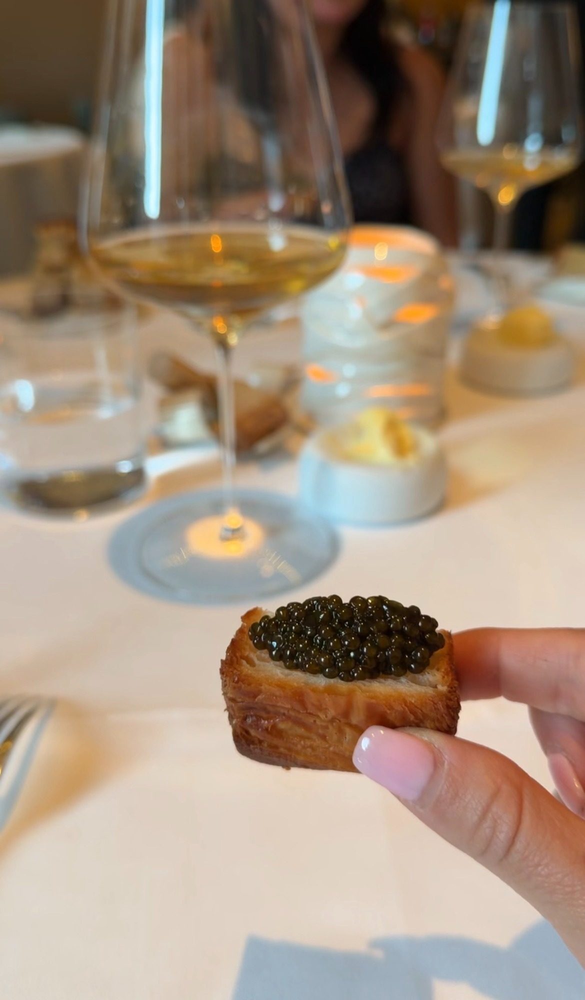Caviar on toasted bread held over a Paris dinner table with white wine