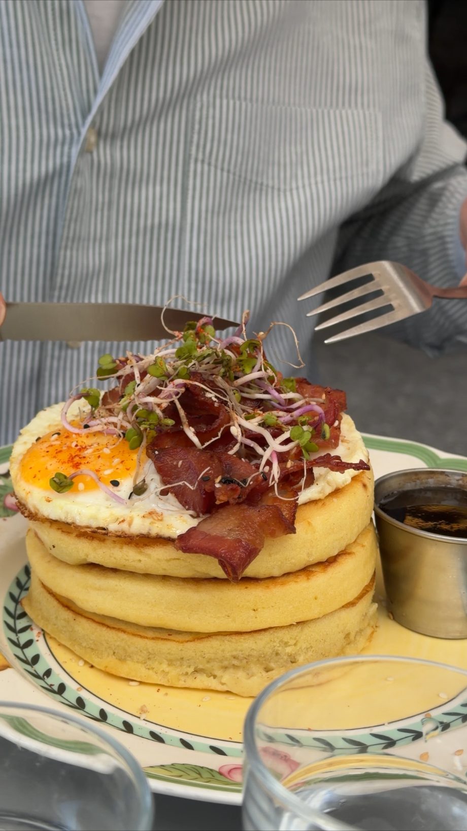 Stack of pancakes topped with bacon, a fried egg, and sprouts at brunch in Paris
