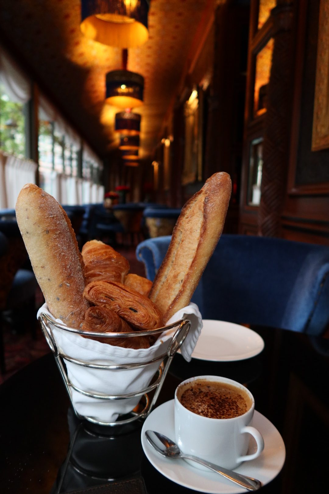 Basket of French baguettes and croissants with coffee in an ornate Paris cafe