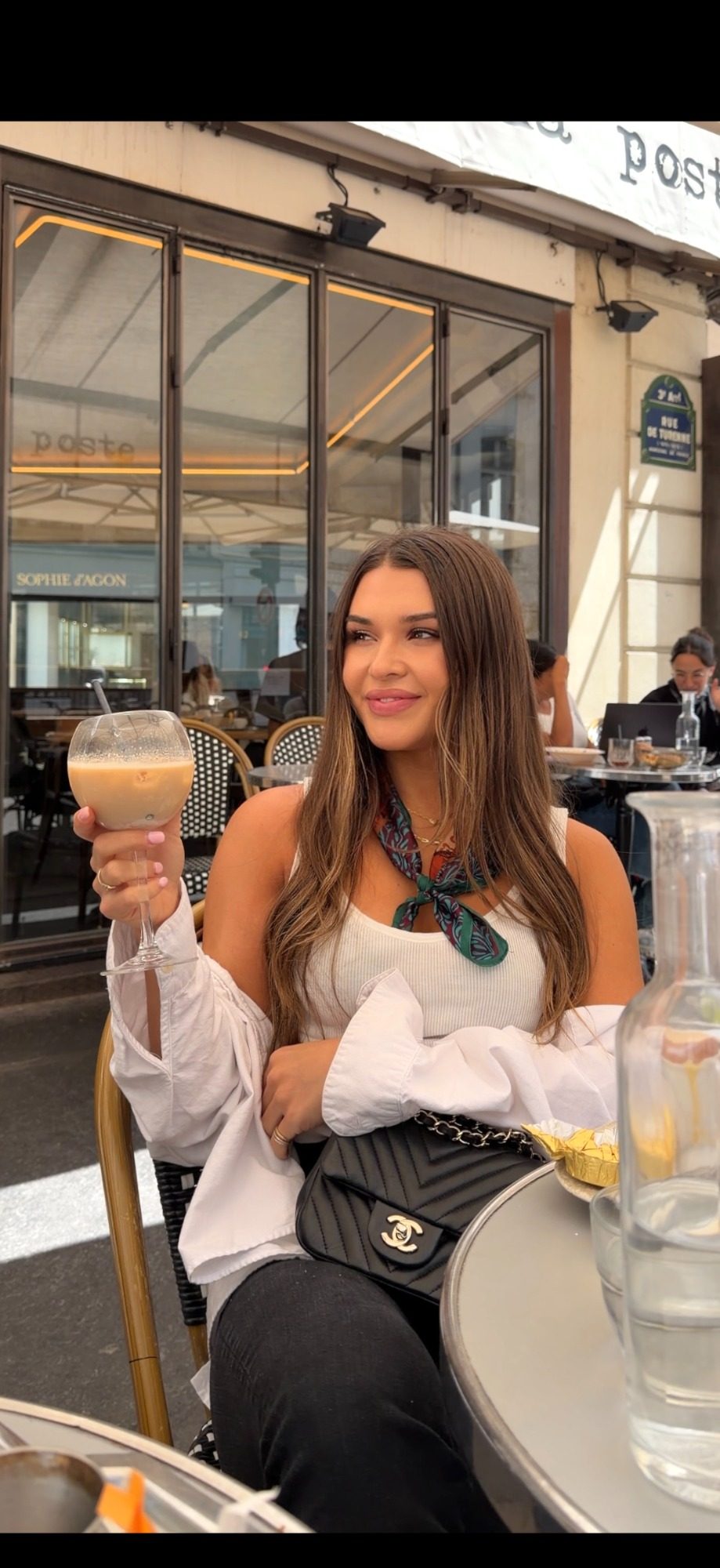 Jess holding an iced coffee at a sidewalk cafe on Rue de Turbigo in Paris